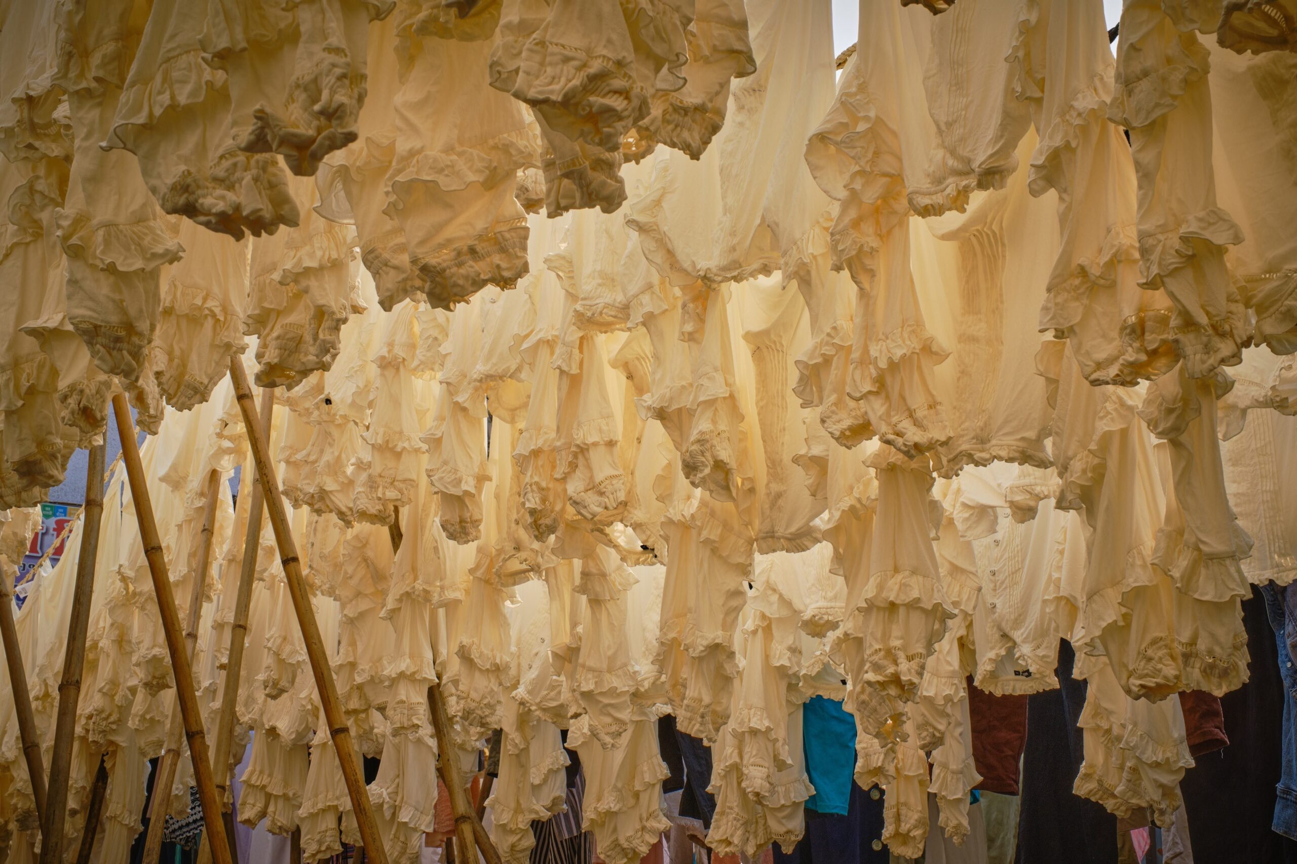 Services White garments hanging outdoors on bamboo poles, creating a textured pattern of clothing.