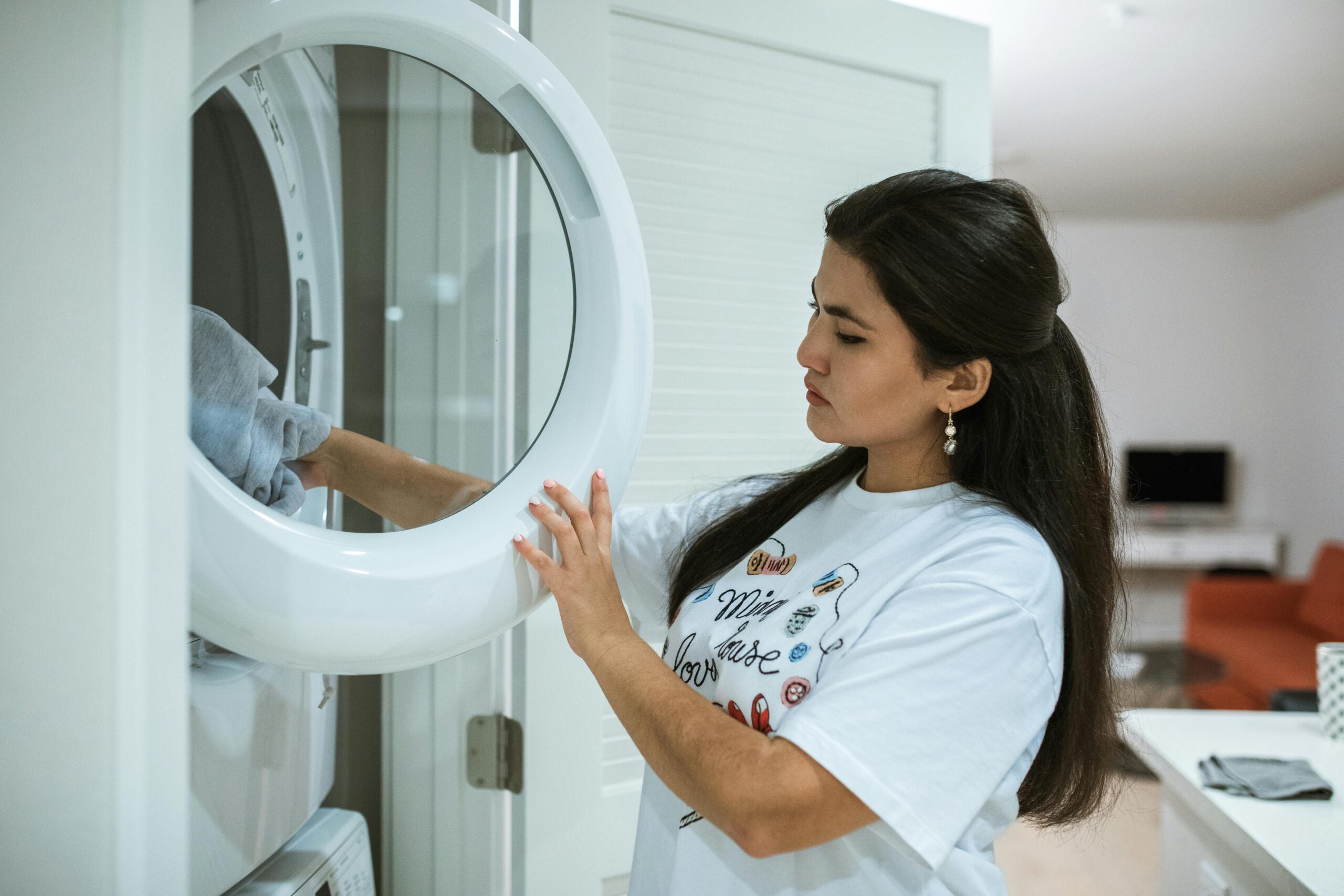Services A woman loads clothes into a modern washing machine, focusing on laundry in a stylish home setting.