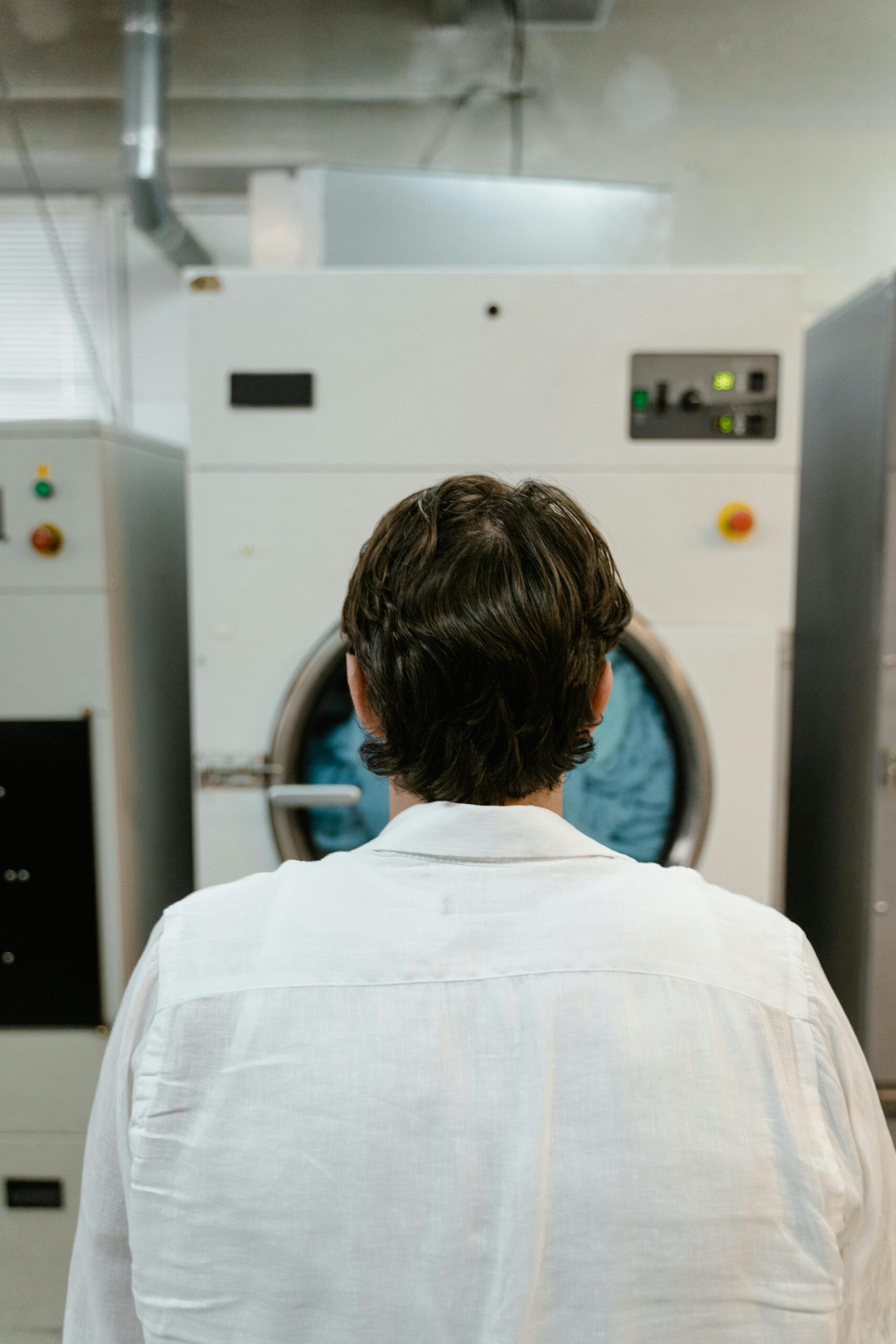dry clean menu Back view of a man operating a large industrial washing machine in a laundry facility.